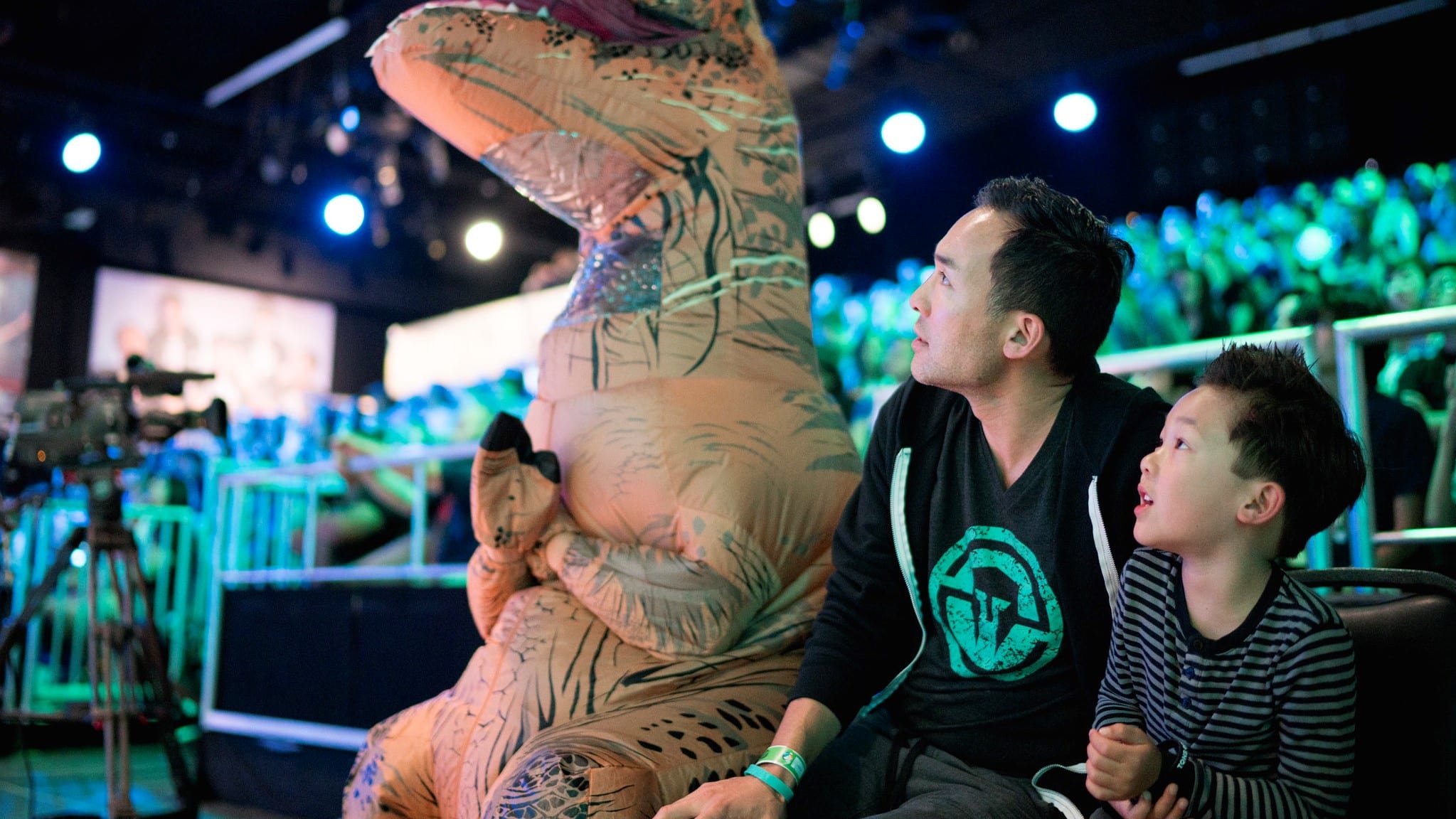 A father and son watch an LCS game in the stands next to a person and an inflatable dinosaur consume