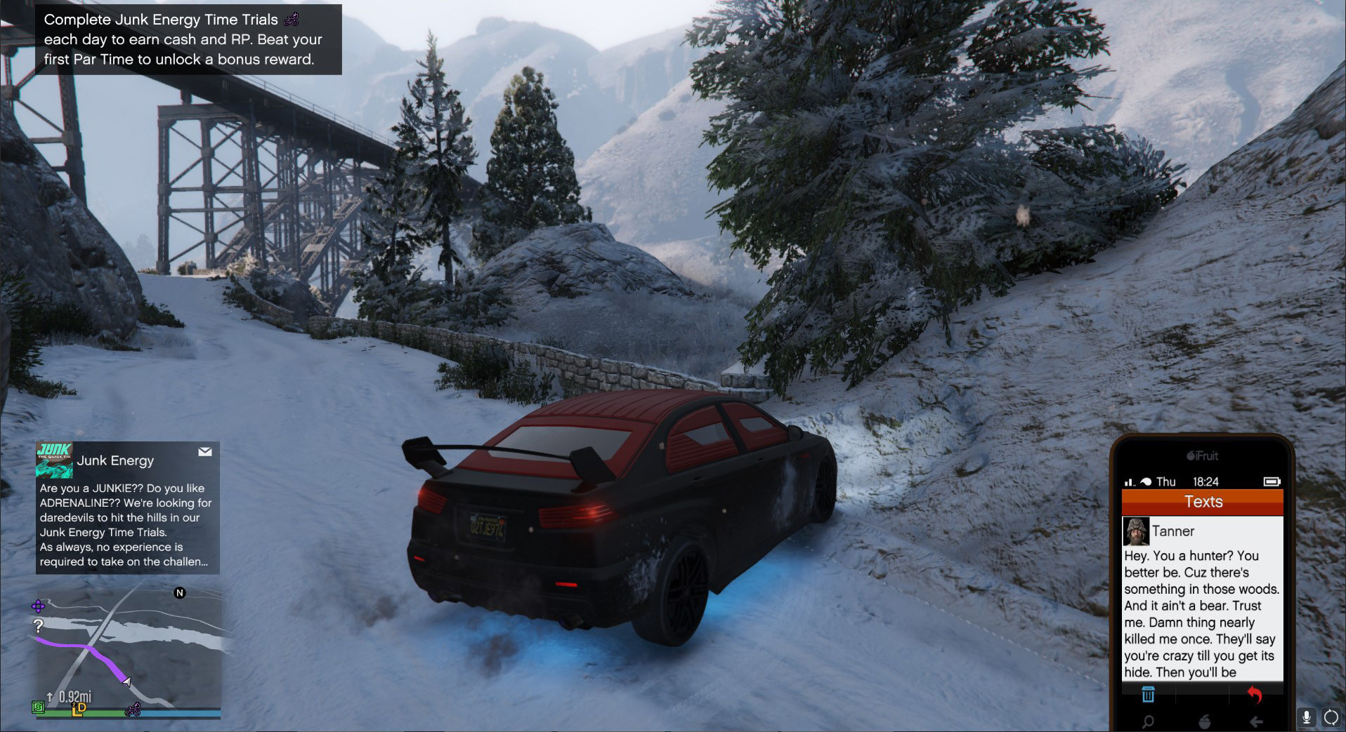 A black and red car on a snowy road, with a stone wall and a big bridge in the background.