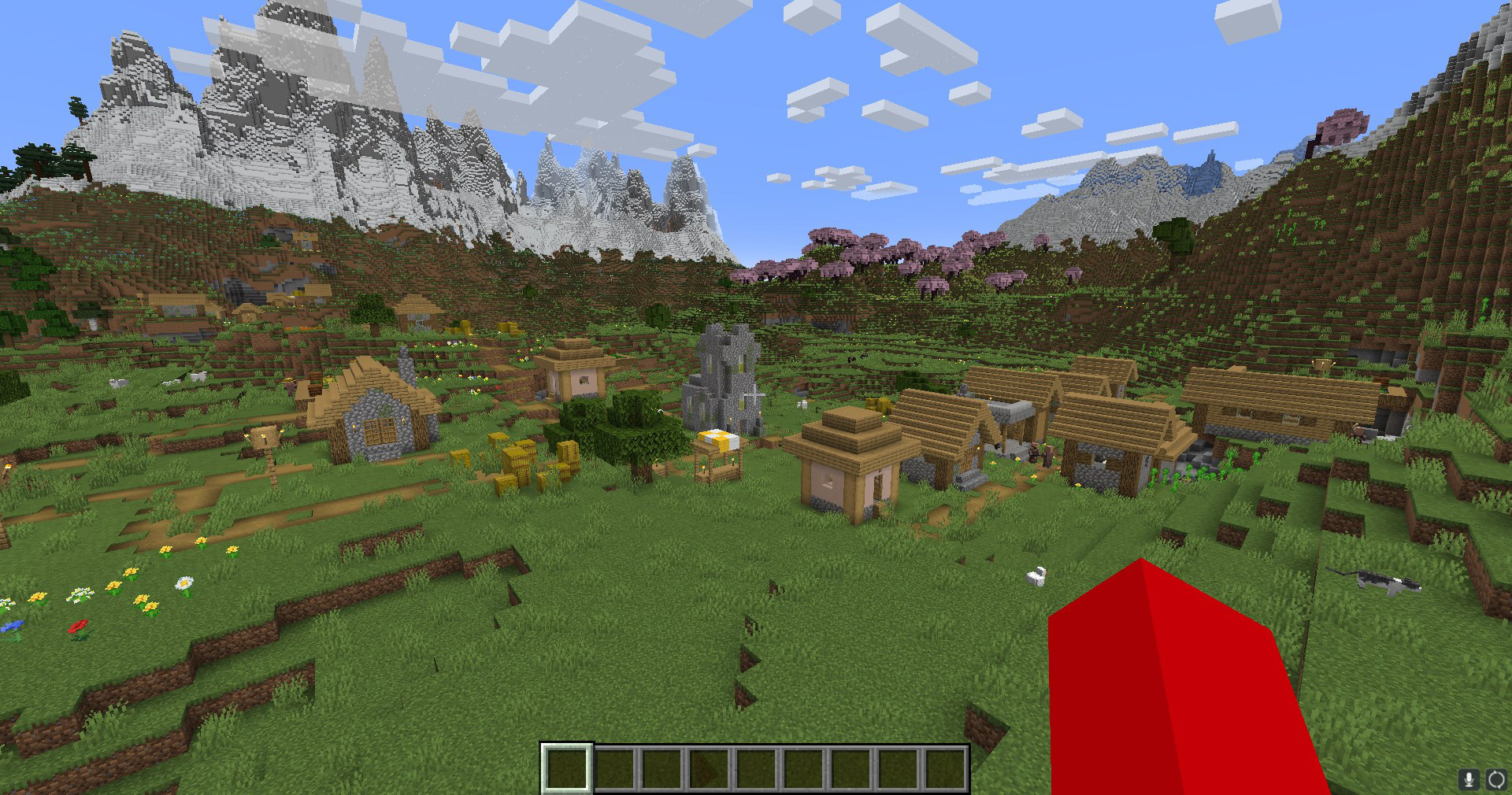 A flying Minecraft player looking at a village with a stone tower. A Cherry Grove biome is behind it, with big snowy mountains further back. 