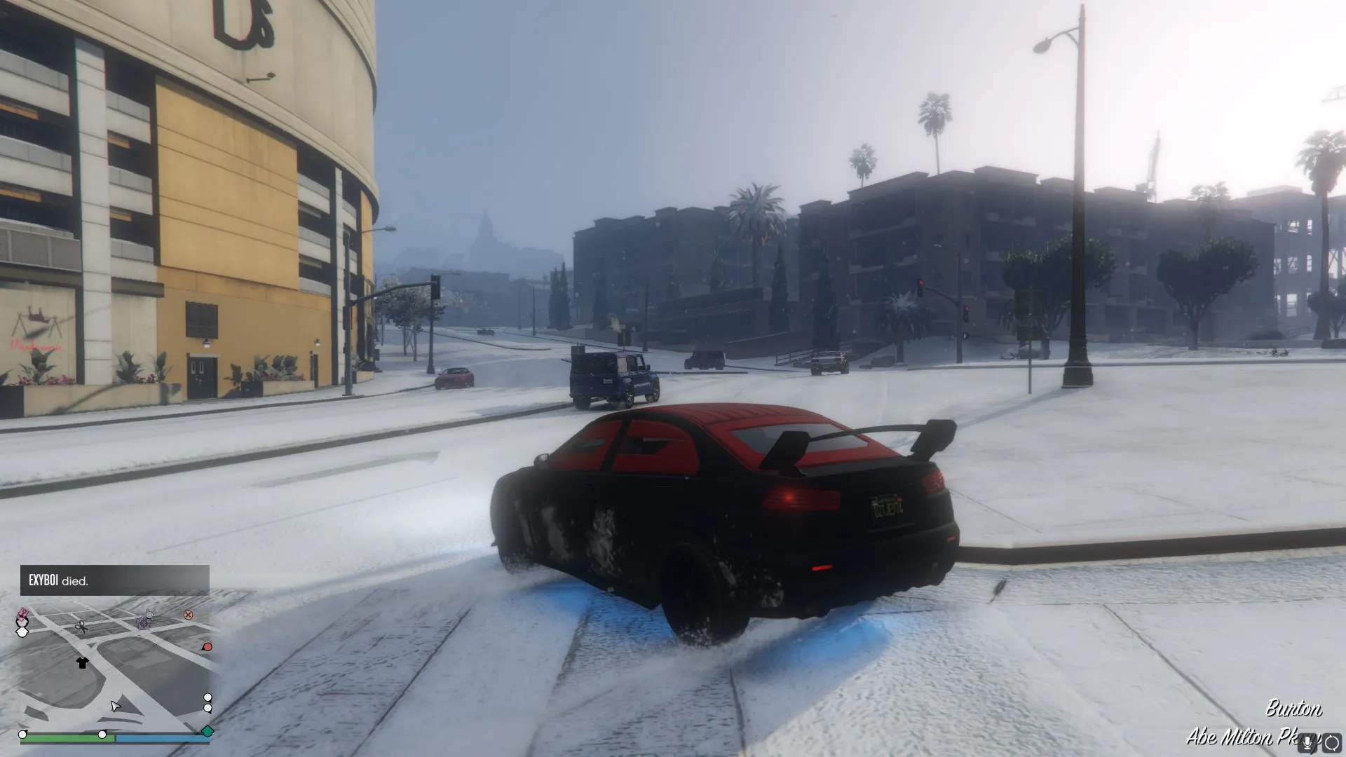A black and red car sliding around a corner covered in snow, about 6 feet away from a lightpost. 