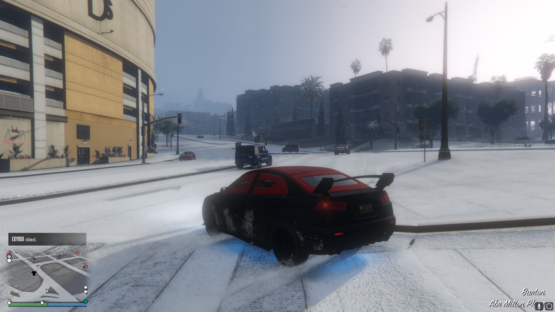 A black and red car sliding around a corner covered in snow, about 6 feet away from a lightpost.