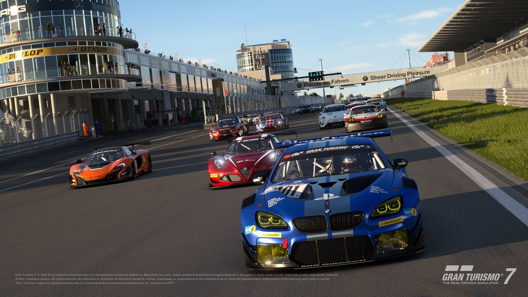 A race at Portimao race track, with cars racing down the finish straight. The lead car is a blue BMW with a PlayStation-themed livery.