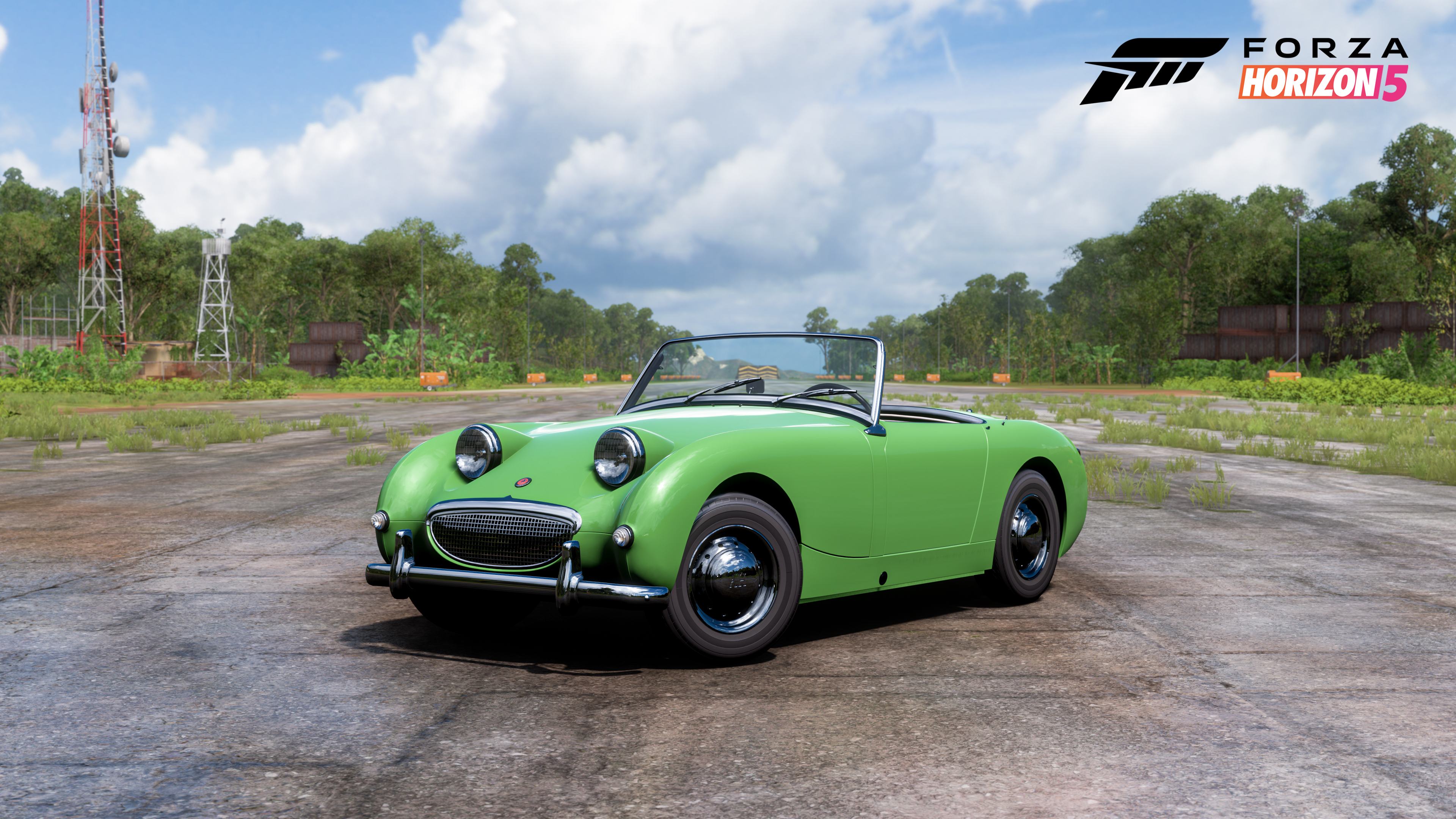 A green Austin Healey Sprite sitting on a tarmac road with trees either side of it.